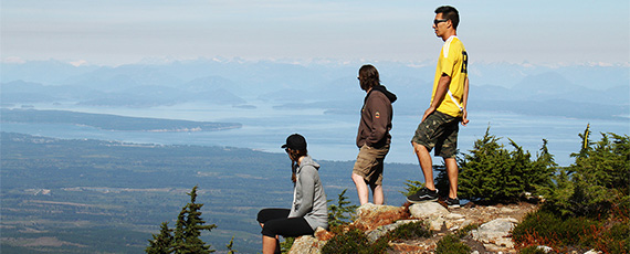 3 people standing near a cliff on Mount Washington looking at the view
